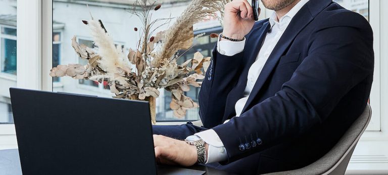 Mand taler i telefon og skriver på laptop