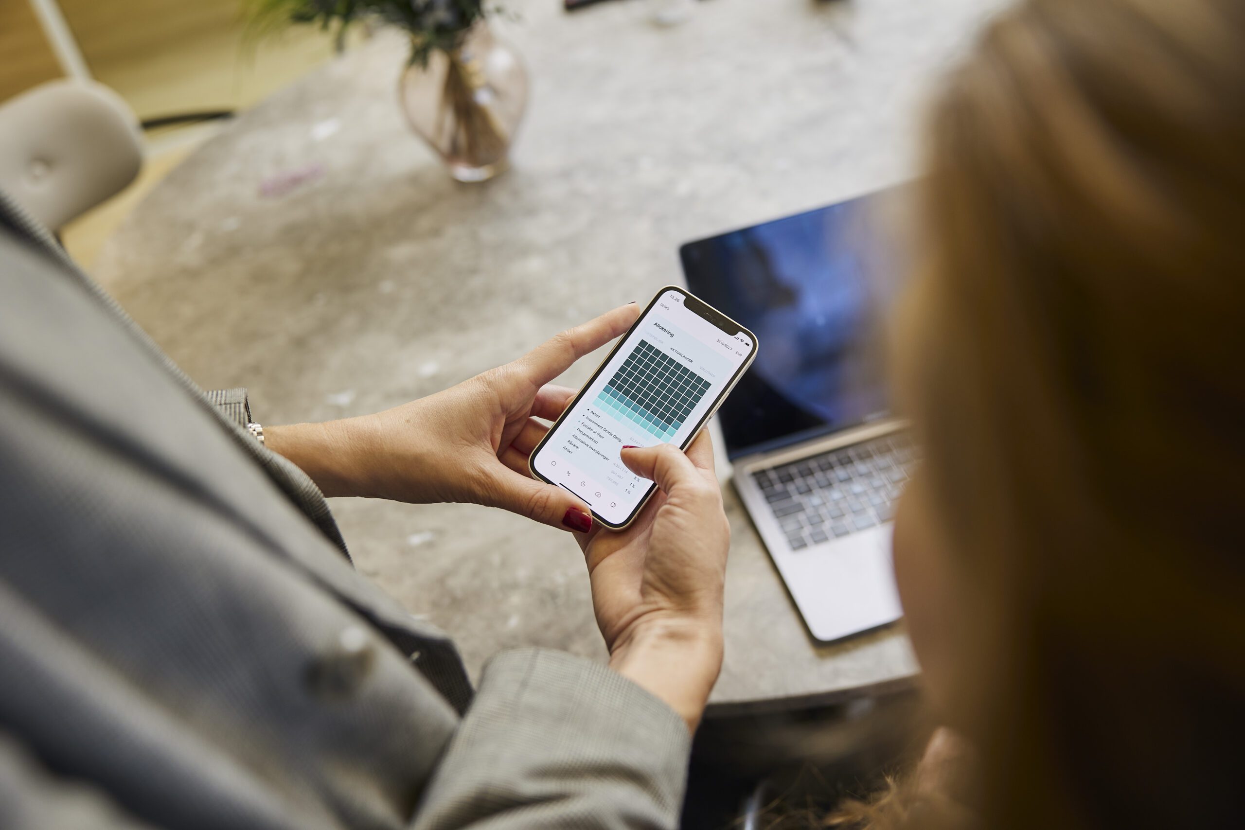 Kvinde bruger investerings-app på telefon foran computer
